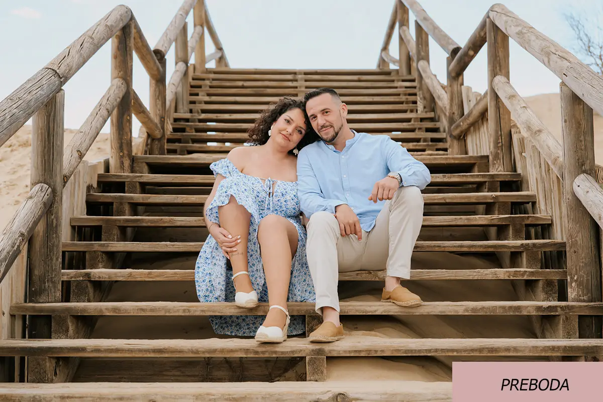 Imagen de una pareja sentada en unas escaleras de madera en la playa